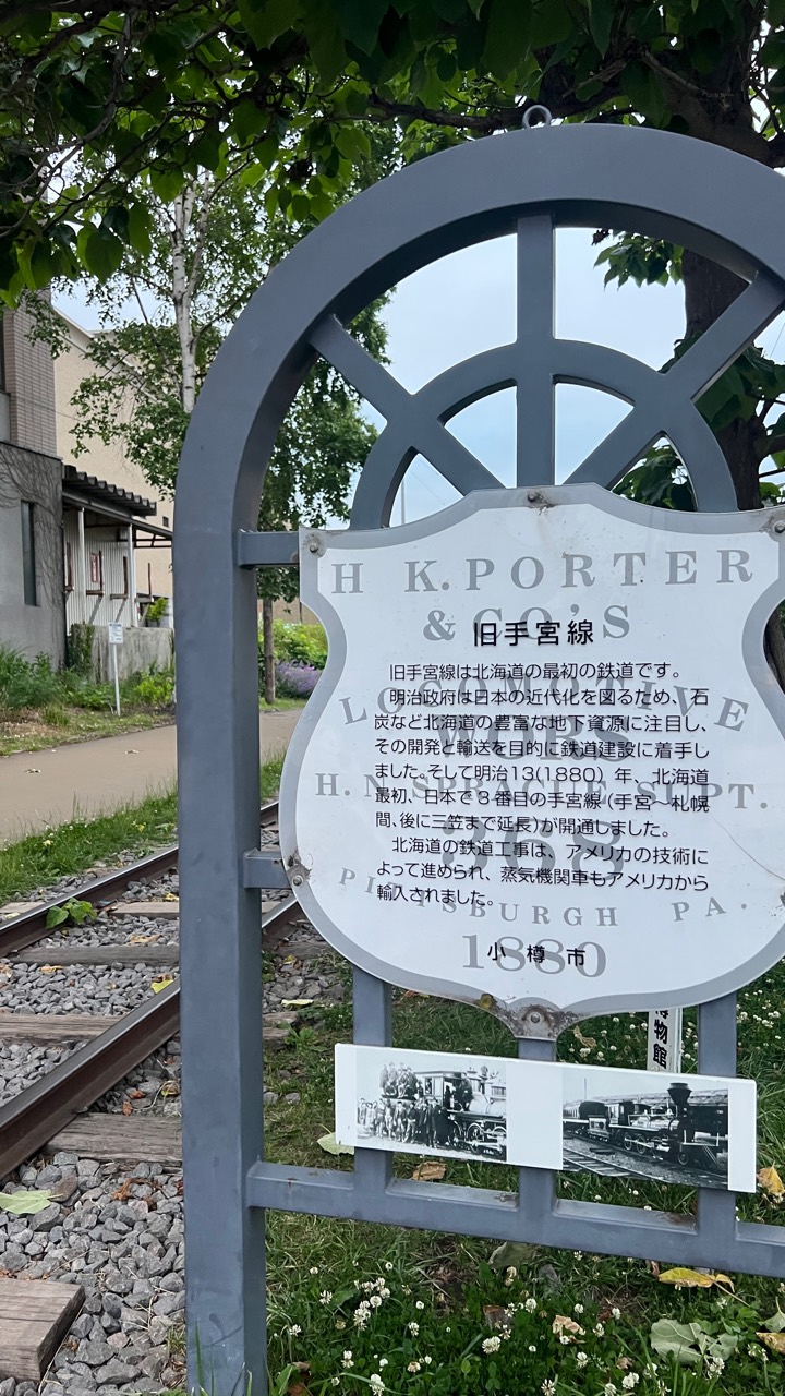 舊手宮線的現地說明牌，外框做成車輪形狀，鑄著「H. K. PORTER & CO'S LOCOMOTIVE, PITTSBURGH PA. 1880」；牌後是仍鑲在路面上的鐵軌與枕木。