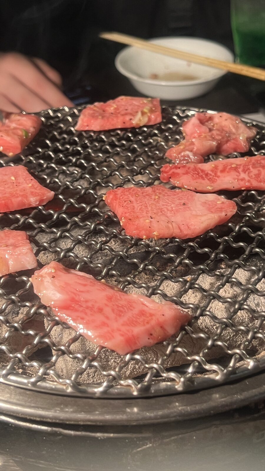 牛肉片鋪在炭火烤網上，邊緣開始捲曲。